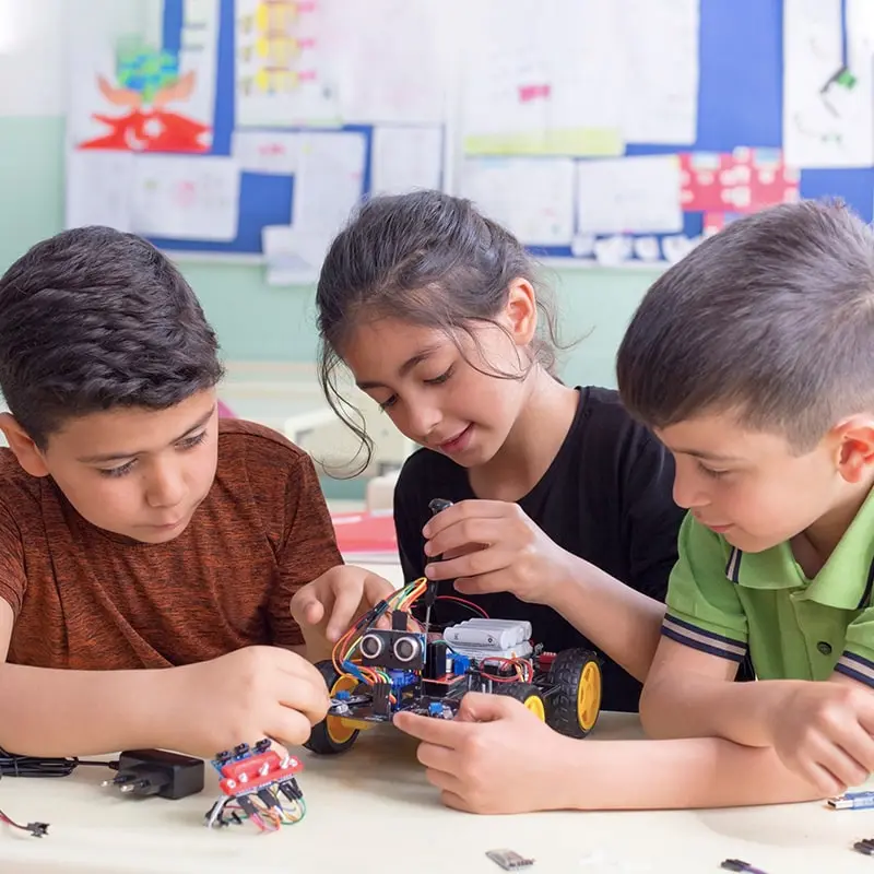 A girl and two boys work together on a robot project in a classroom.
