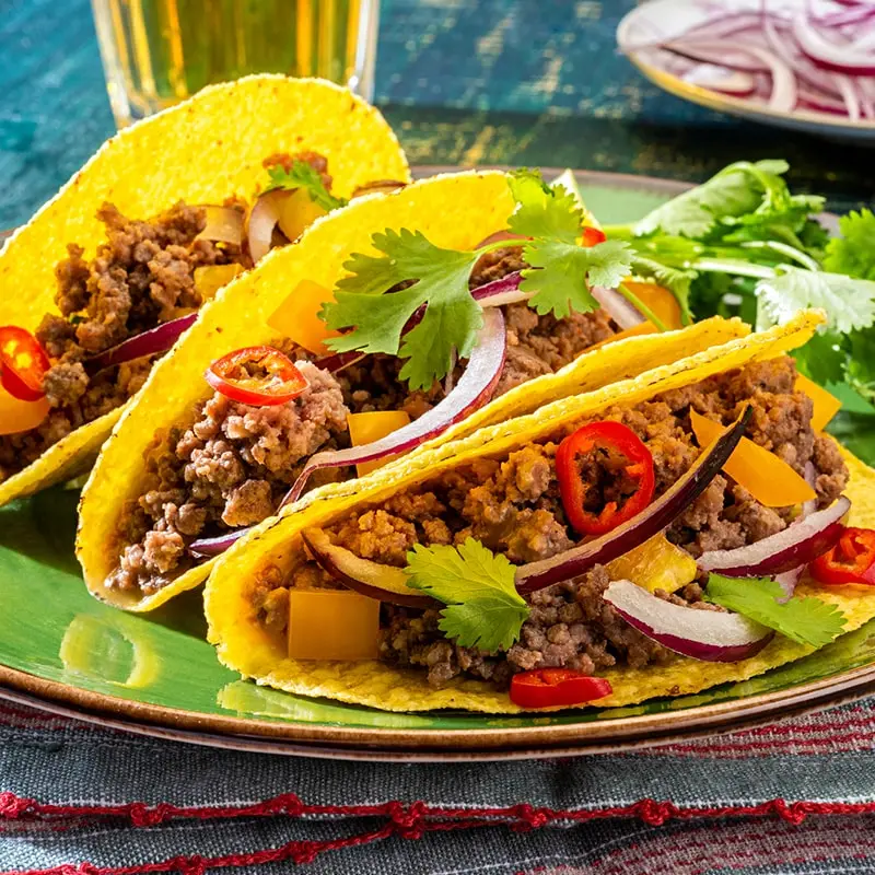 Three crunchy beef tacos on a green plate.