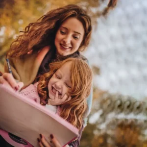 A young woman and her daughter sit outside during the fall coloring together.