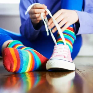 A young child wearing rainbow stripes socks is tying their shoelaces.