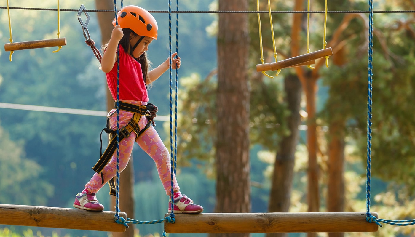 A young girl is walking on a rope bridge at an adventure park.