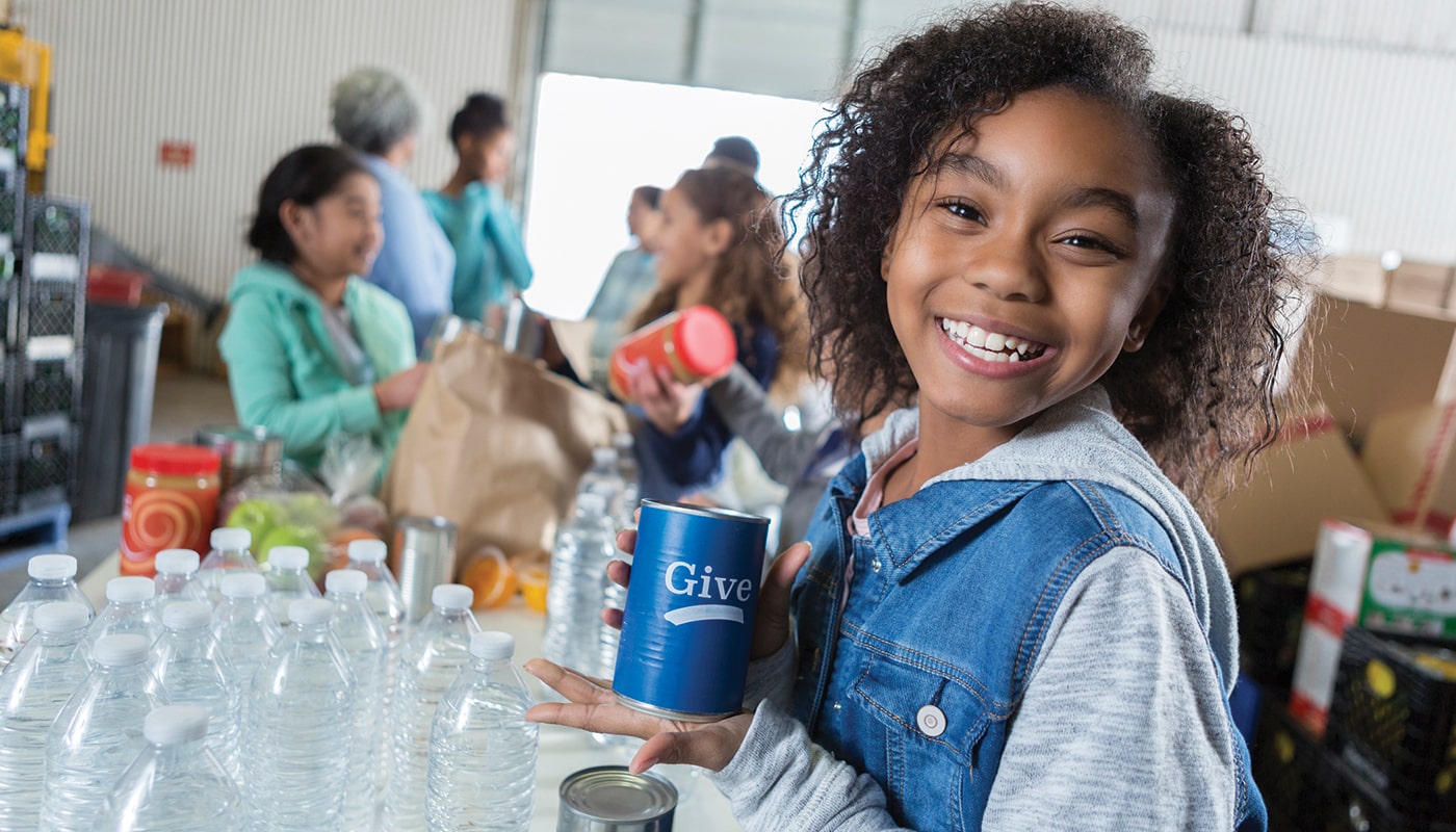 A young girl volunteering at a food bank encourages us to donate.