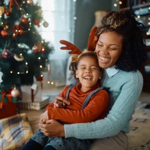 A mom and her son laugh at a joke together in front of a Christmas tree.