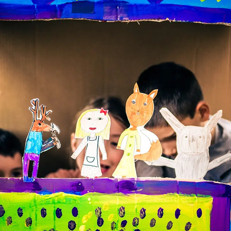 Two children put on a puppet show with paper puppets on sticks.