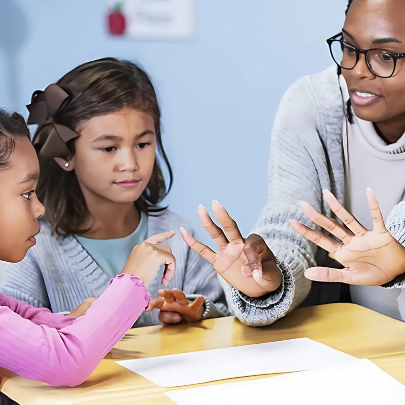 A teacher sits with two young students who are learning to count.